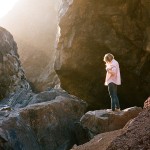 photograph of a woman standing on a rocky outcrop at sunset