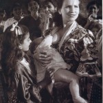 black & white period picture of a group of women and one woman breastfeeding a baby