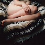 photograph of a woman on an armchair with legs tucked together