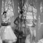 black and white photo of two models in a window with sculptures and trees reflected in the glass