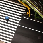 aerial photo of a man with a blue umbrella crossing zebra lines