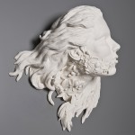 White porcelain bust of a woman's face with flowing hair, flora growing out of her neck.