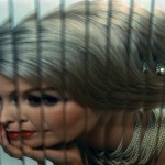blonde woman with coiffed hair, pearls, red lipstick and nails as reflected through an array of mirror strips