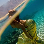 Topless woman standing in a shallow lagoon wearing a golden cloth around her waist and poking her head above the water.