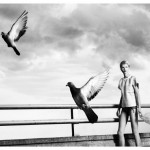 model walks by rail as pigeons fly past