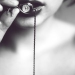 Woman pressing a small chained pocket watch between her lips.