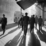 men walking towards the sun on a street near a double decker bus