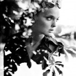 woman with scarf and sunglasses seen through window with reflection of tree leaves