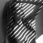 nude woman against wall with slats of light through blinds