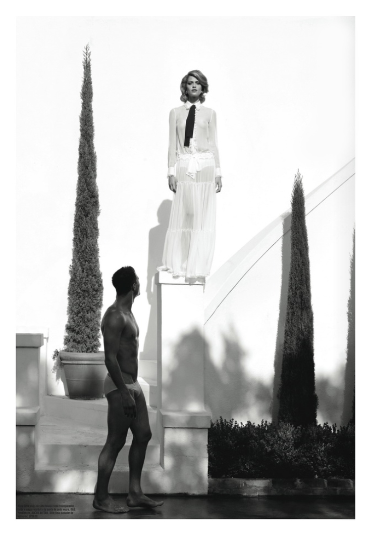 black & white picture of a woman standing on a pedestal while a man in underwear looks on from below