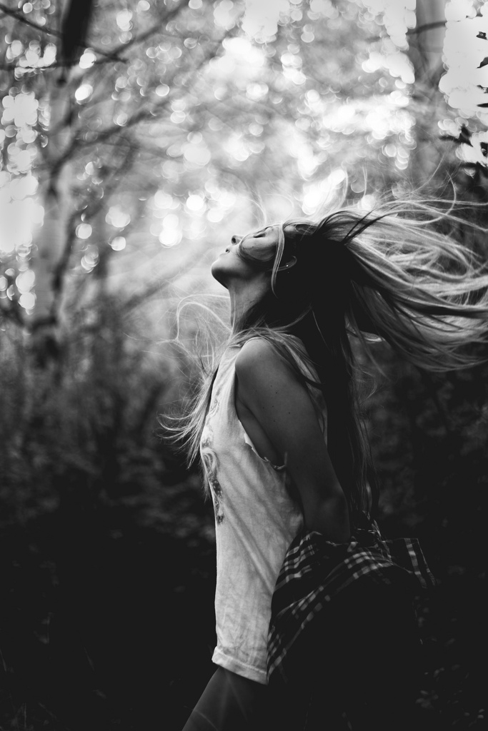 Black & white photo of a young woman tossing her hair back in a woodland area