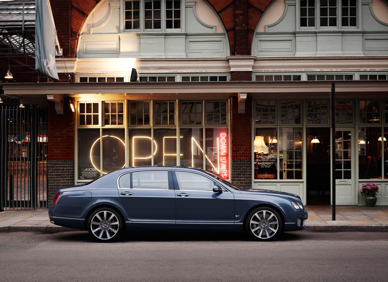 Blue Bentley Continental Flying Spur in front of a shop with a large OPEN sign