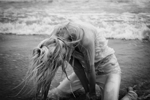 Black & white photo of a blonde woman by the beach with waves