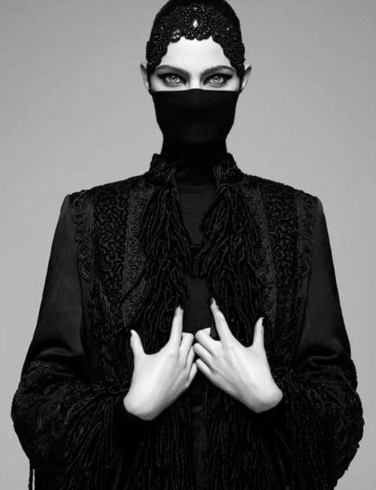 Fashion shoot photograph of a woman covered in black clothing except her hands and eyes