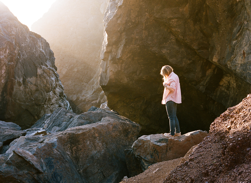 photograph of a woman standing on a rocky outcrop at sunset