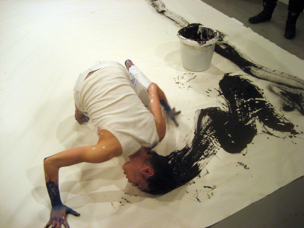 photograph of performance art of a woman painting with her hair