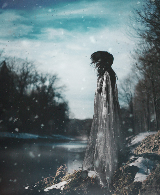 photograph of a woman next to water in a winter woodland