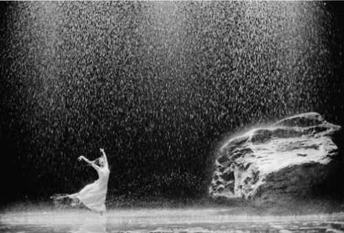 black & white photo of a ballet dancer on a stage filled with water, rain and rocks