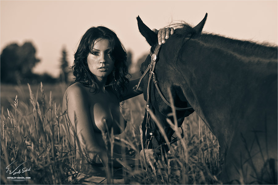 Sepia photograph of a topless woman in a field with a horse.