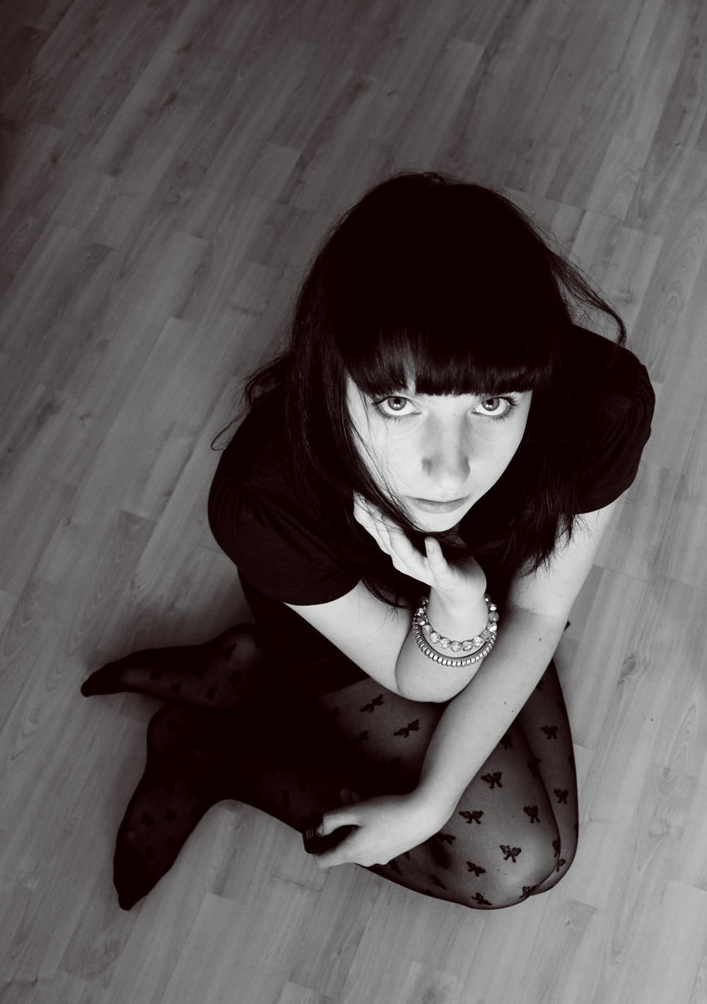Girl in black dress on wood flooring looking up at the camera.