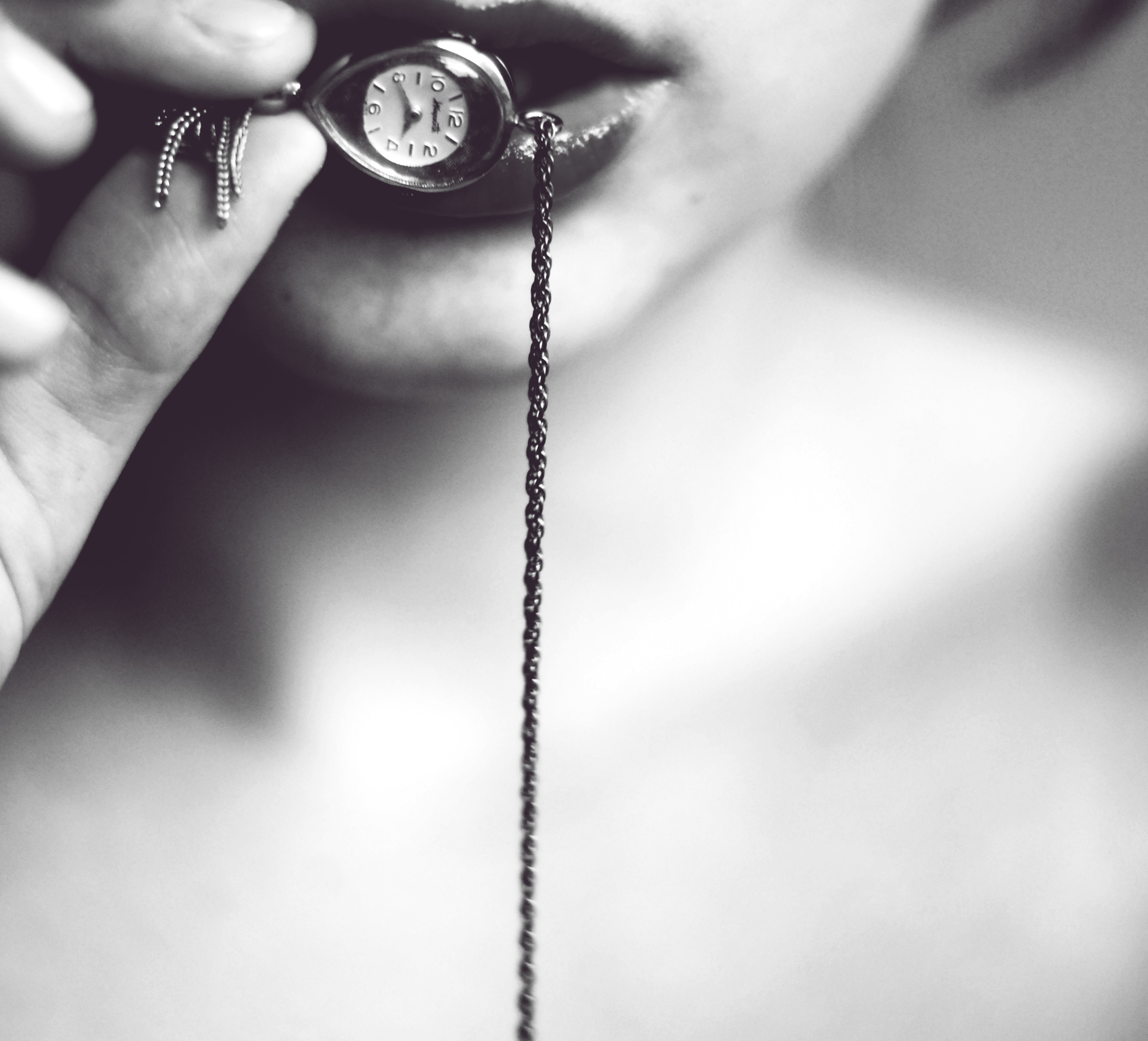 Woman pressing a small chained pocket watch between her lips.