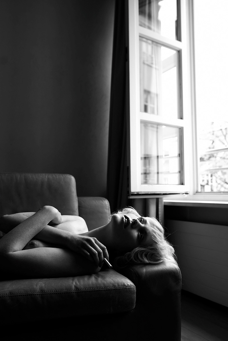 Nude woman lying down on a couch next to a window