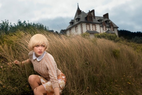 sophie vlaming crouched in grass near house, wide shot