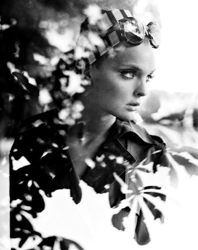 woman with scarf and sunglasses seen through window with reflection of tree leaves