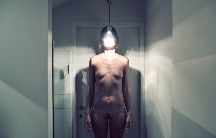 A naked light bulb hanging in front of the face of a naked woman - Annalaura Masciavè Photography